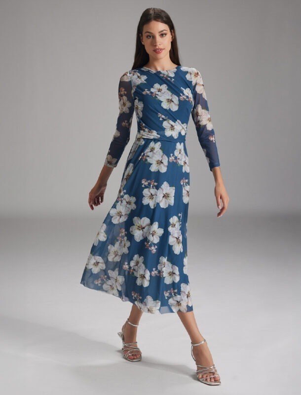 Eine Frau in einem blauen, blumigen Kleid mit langen Ärmeln, die auf einem neutralen Hintergrund steht. Eine Frau in einem blauen, blumigen Kleid mit langen Ärmeln, die auf einem neutralen Hintergrund steht.