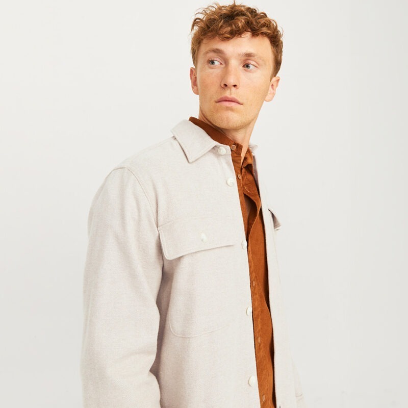 Ein Mann mit lockigem, blonden Haar trägt eine hellbeige Jacke über einem braunen Hemd. Er schaut zur Seite. Ein Mann mit lockigem, blonden Haar trägt eine hellbeige Jacke über einem braunen Hemd. Er schaut zur Seite.