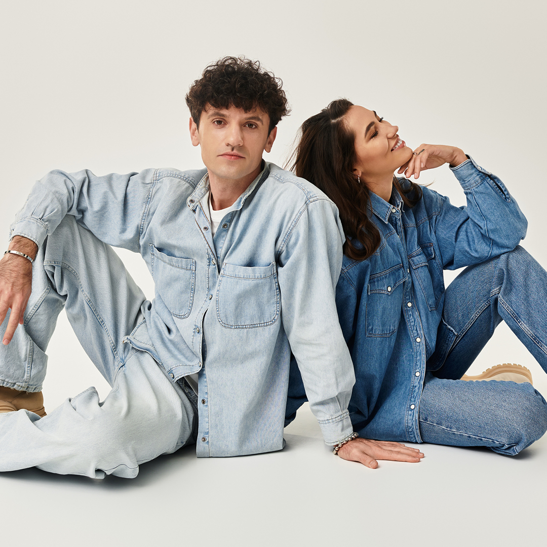 Ein Mann und eine Frau sitzen auf dem Boden, sie tragen Jeanshosen und Jeanshemden sowie beige Boots. Ein Mann und eine Frau sitzen auf dem Boden, sie tragen Jeanshosen und Jeanshemden sowie beige Boots.