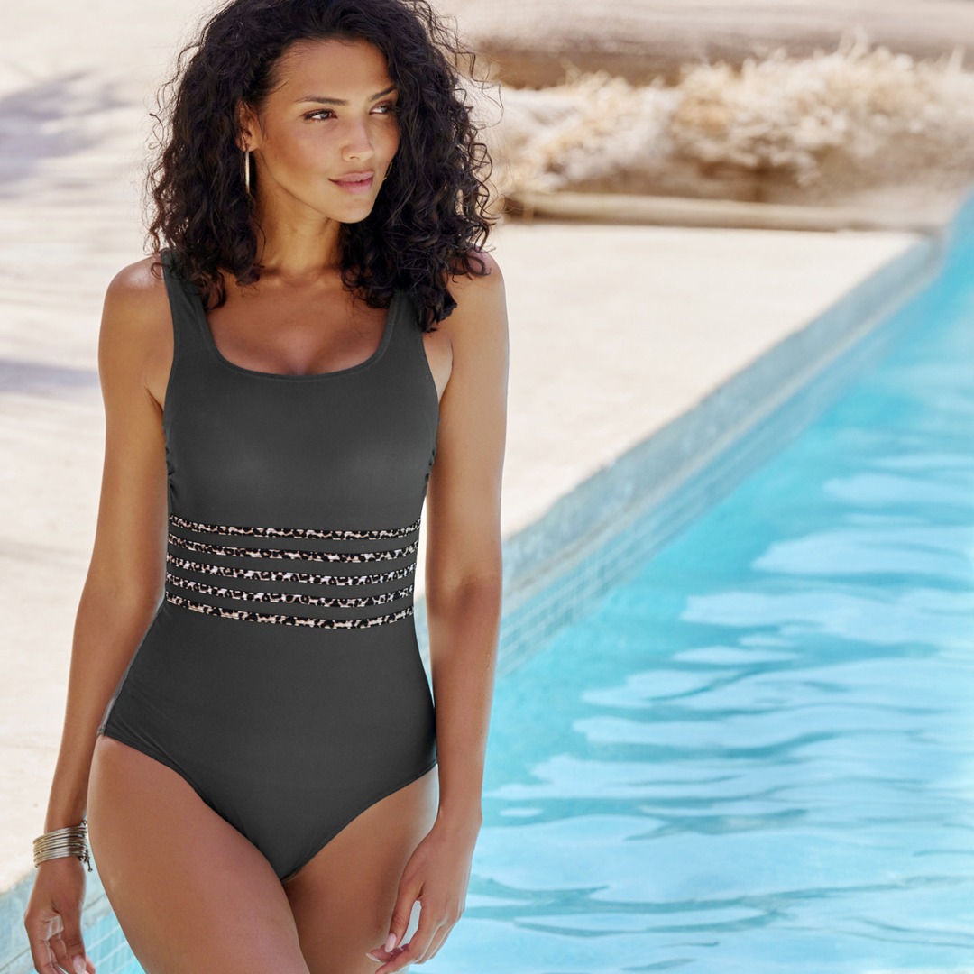 Am Pool steht eine Frau in einem eleganten schwarzen Badeanzug. Am Pool steht eine Frau in einem eleganten schwarzen Badeanzug.