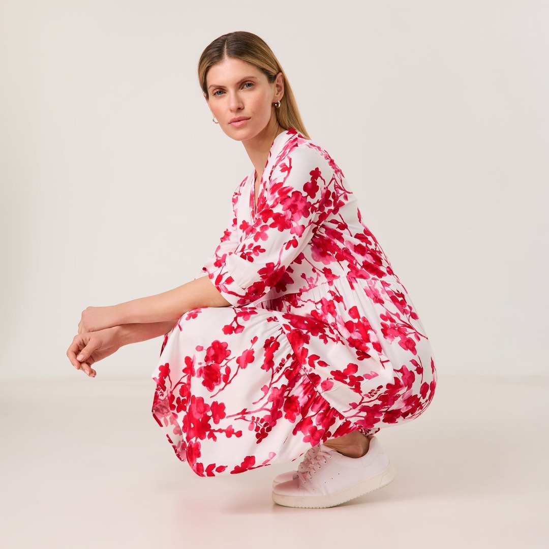 Eine Frau in einem rot-weißen Blumenkleid sitzt auf dem Boden.