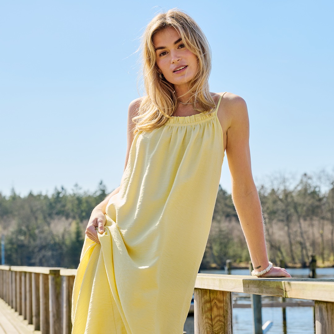 Eine Frau trägt ein gelbes Kleid und steht auf einer Wiese.