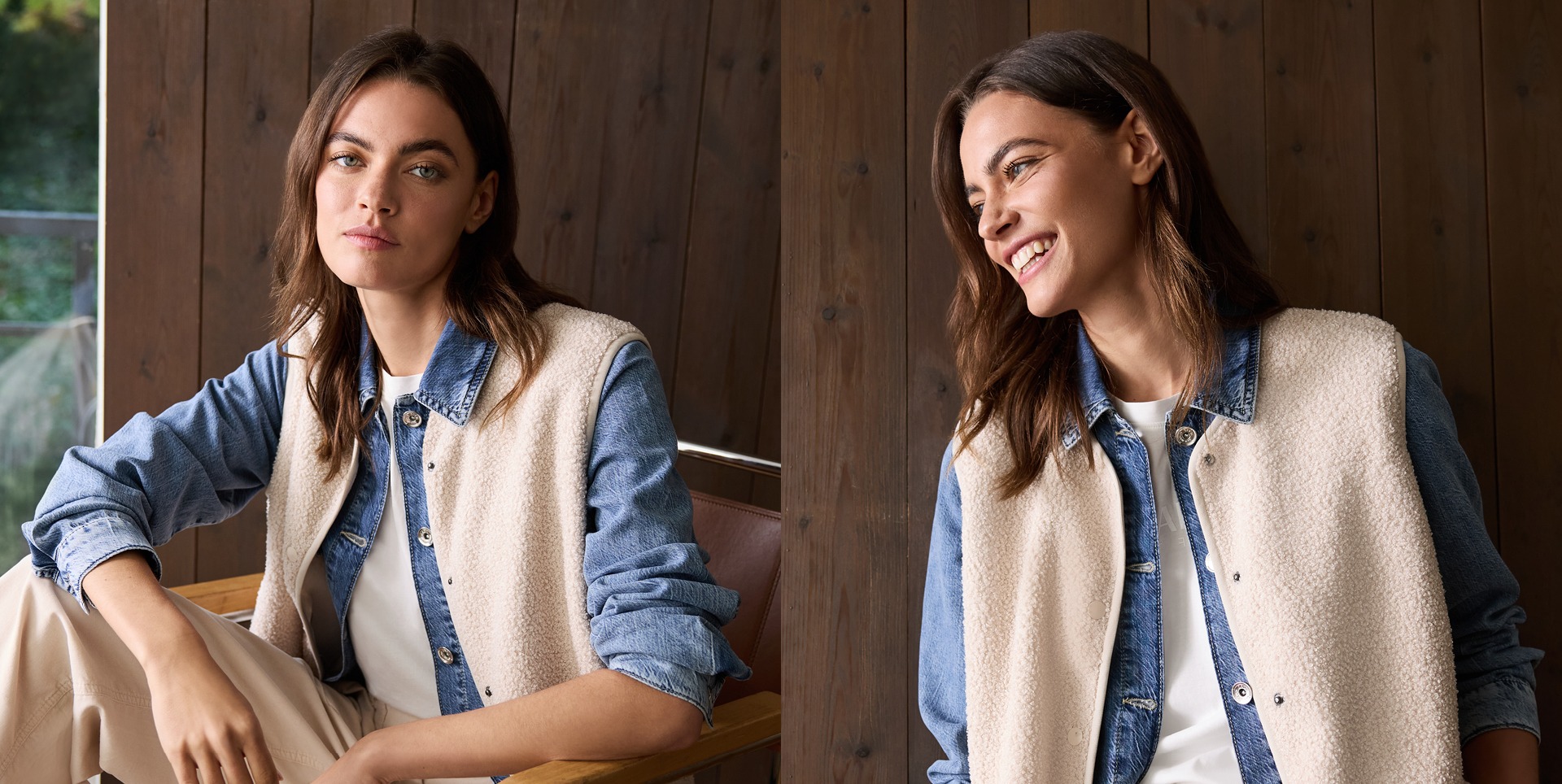 Eine Frau sitzt in einem Holzgebäude, trägt eine Jeansjacke und eine helle Weste. Sie hat braune Haare und lächelt.