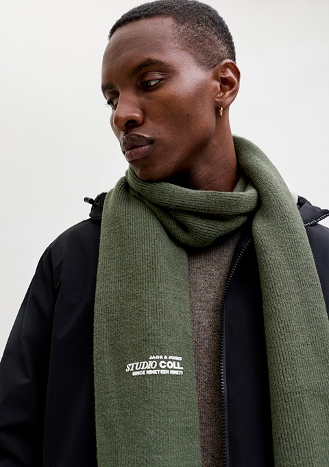 Ein Mann trägt einen grünen Schal und eine schwarze Jacke.