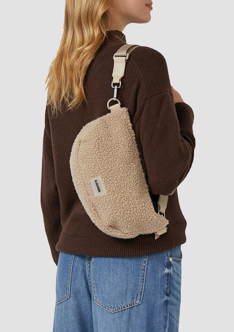 Frau von hinten mit hellbeiger, halbrunder Teddy-Umhängetasche und braunem Pullover, blaue Jeans.