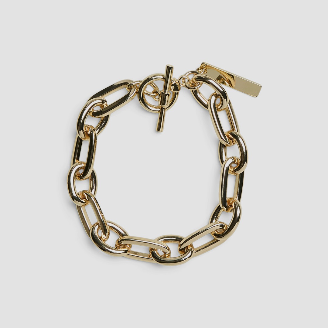 Goldfarbene Gliederkette mit rundem Knebelverschluss und rechteckigem Anhänger auf hellem Untergrund.