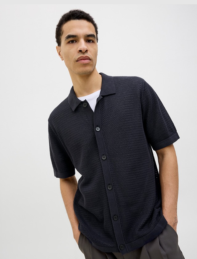 Ein junger Mann trägt ein schwarzes, kurzärmliges Hemd und schaut in die Kamera. Ein junger Mann trägt ein schwarzes, kurzärmliges Hemd und schaut in die Kamera.