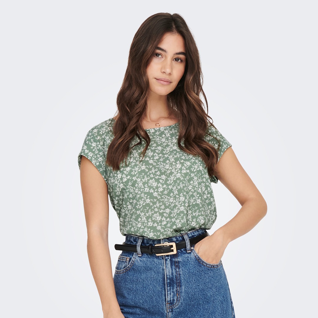 Eine junge Frau trägt ein grün mit Blumenmuster bedrucktes Oberteil und eine blaue Jeans. Eine junge Frau trägt ein grün mit Blumenmuster bedrucktes Oberteil und eine blaue Jeans.